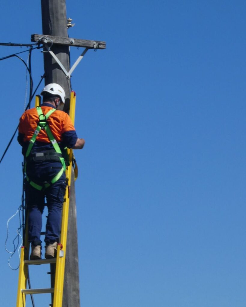 Man wearing safety harness high up on pole